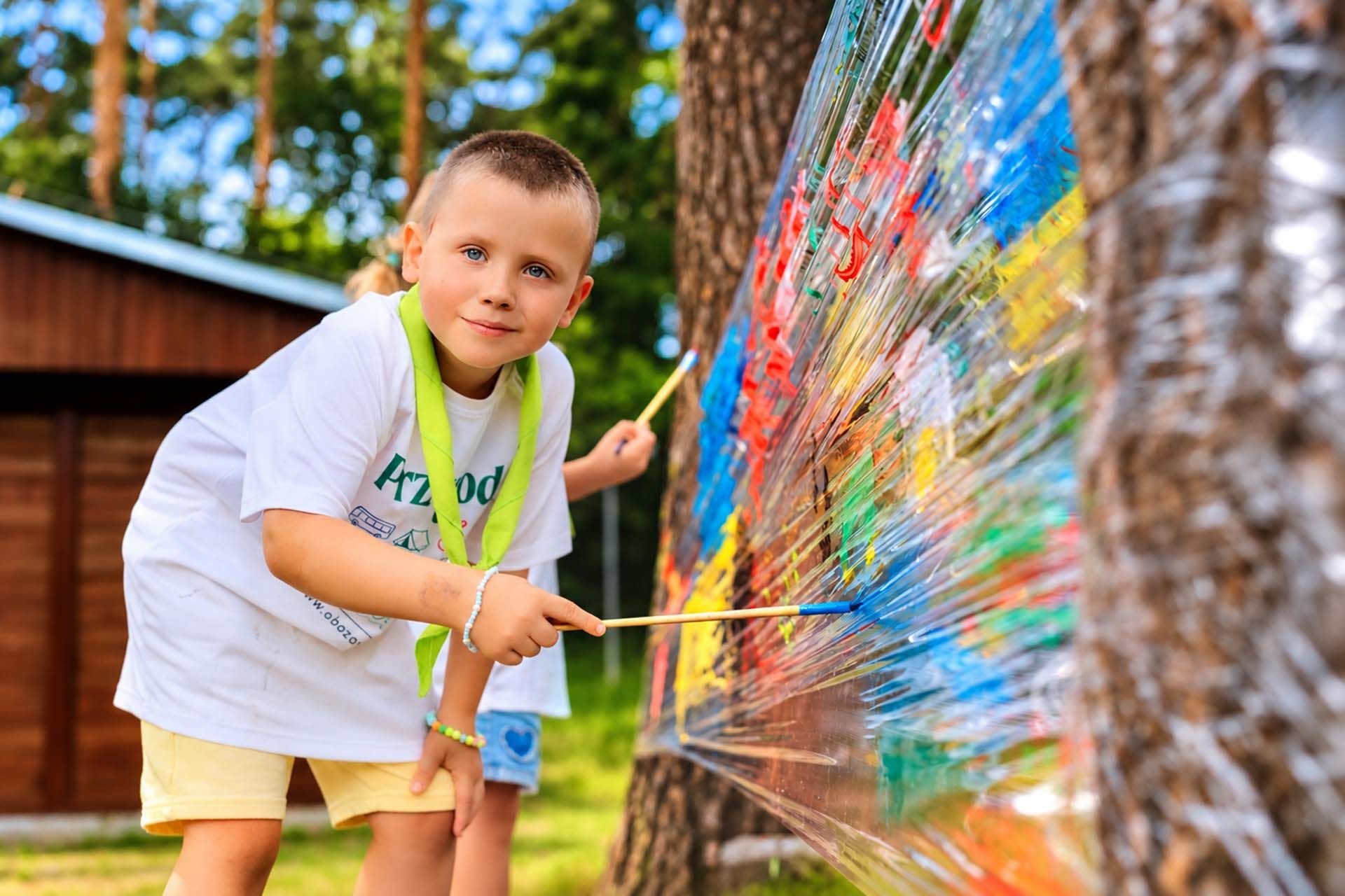 Chłopiec maluje farbami na folii w lesie na Kids Camp w Smerzynie