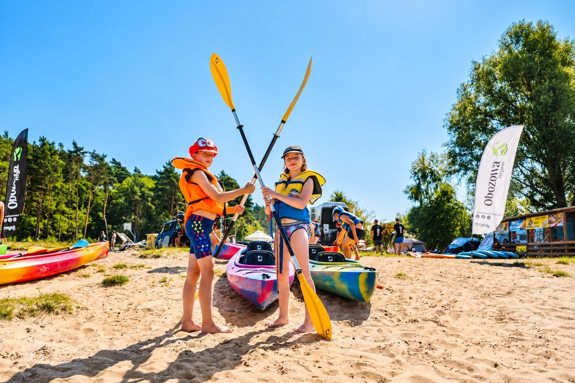 Dzieci z wiosłami na plaży w Smerzynie, w tle kajaki