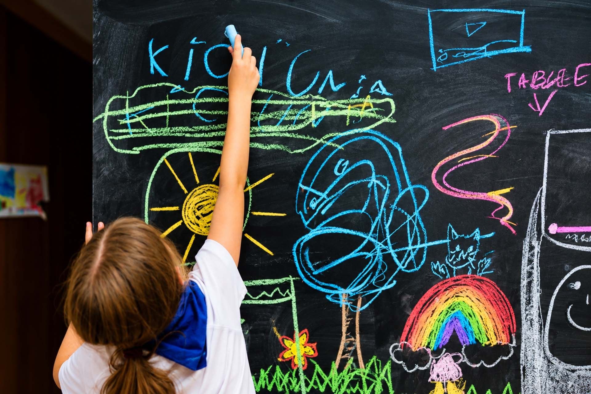 Dziewczynka pisze kredą napis Kids Camp na tablicy