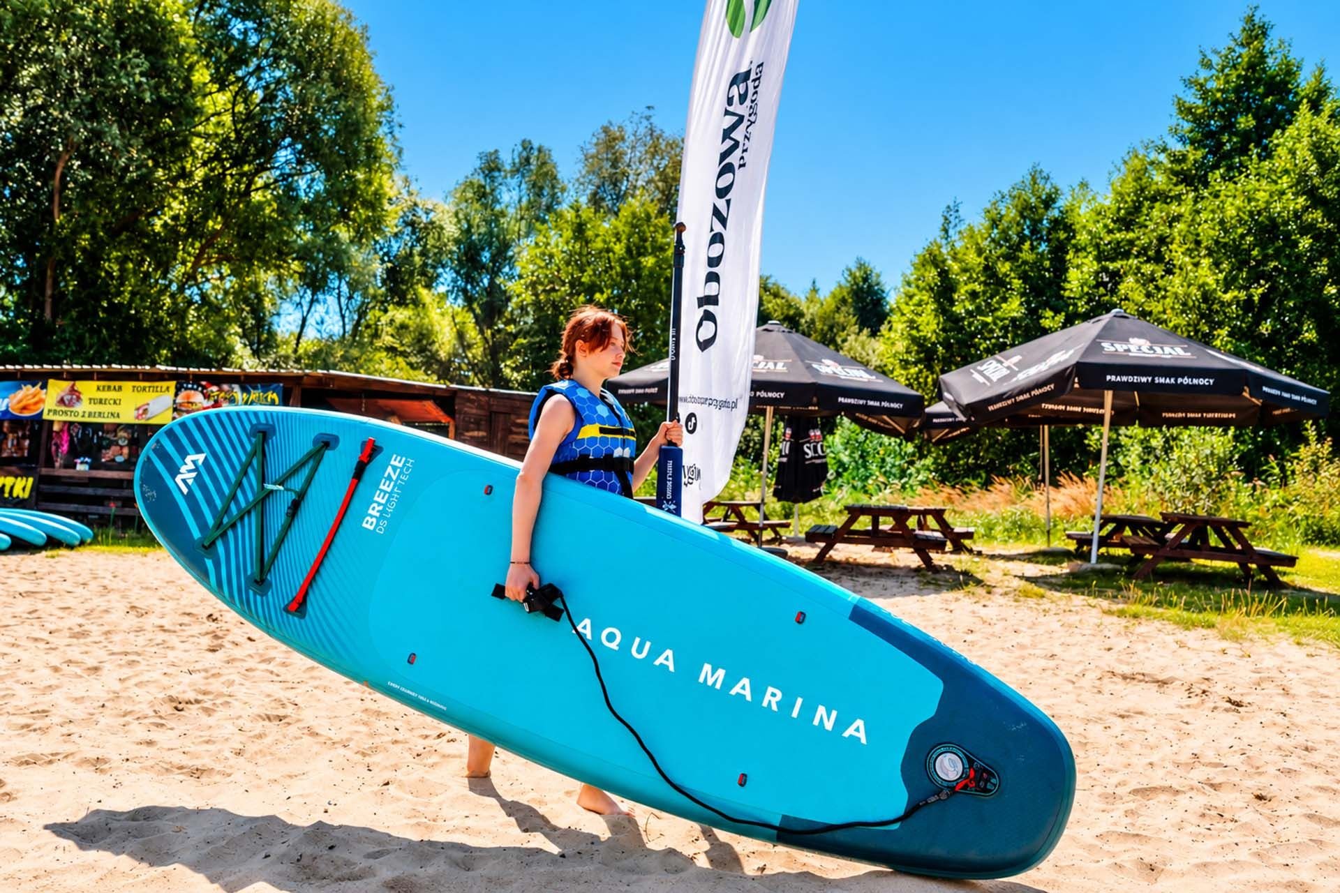 Dziewczynka niesie deskę SUP po plaży w Smerzynie