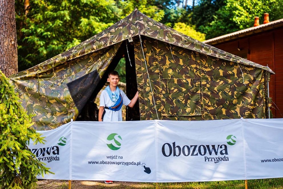 Namiot w Smerzynie, chłopiec stojący w namiocie, przed nim parawan obozowej przygody