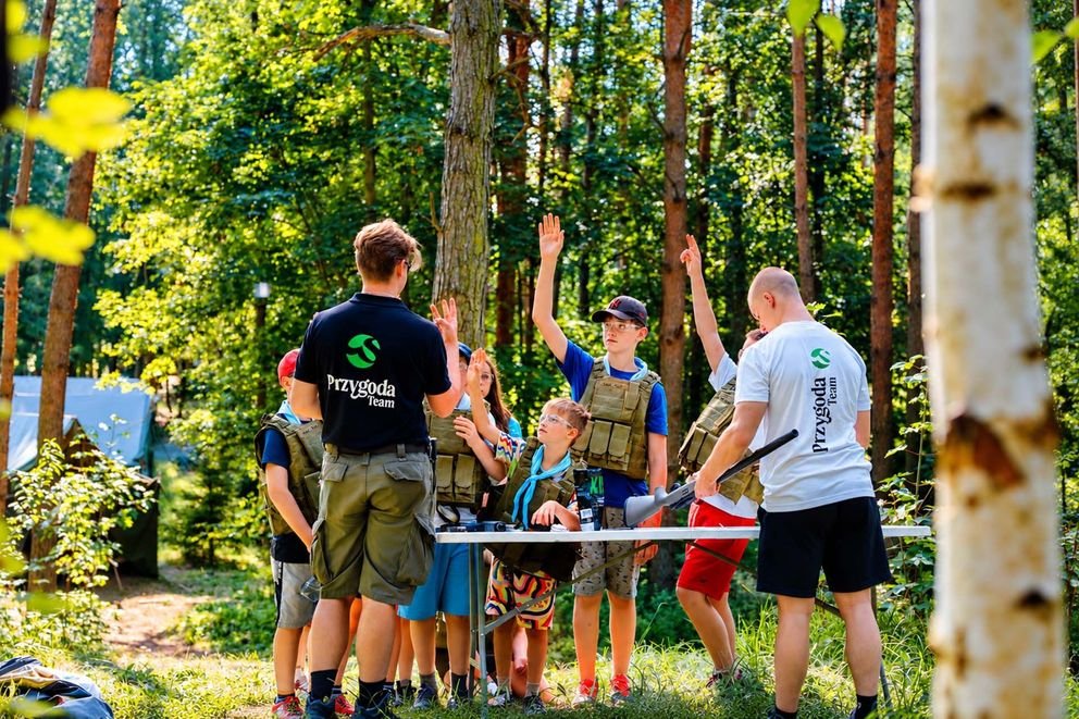 Zajęcia strzeleckie z ASG w Smerzynie dzieci stoją przy stoliku i słuchają instruktora