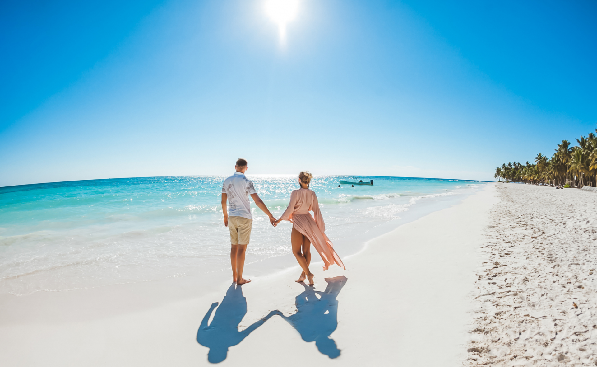 Para trzymająca się za ręce spacerująca na miękkim białym piasku wzdłuż linii brzegowej