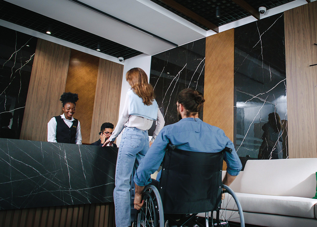 Kobieta i mężczyzna na wózku inwalidzkim obsługiwani przy ladzie recepcyjnej