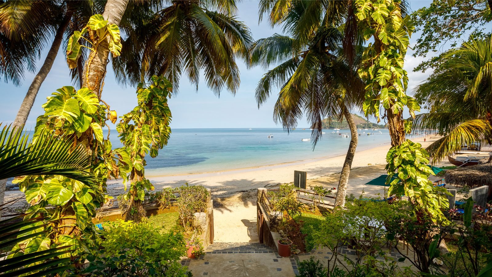 Droga do rajskiej plaży Nosy Be z parasolami i leżakami, w tle turkusowe morze.