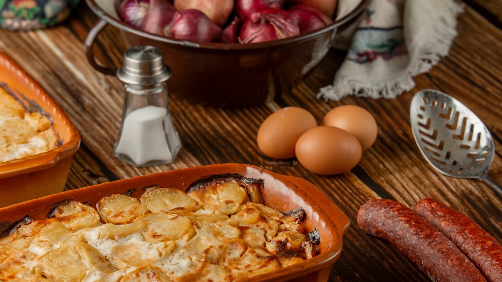 Rakott Krumpli, tradycyjne węgierskie jedzenie na drewnianym tle - warstwowa zapiekanka  ziemniaczana