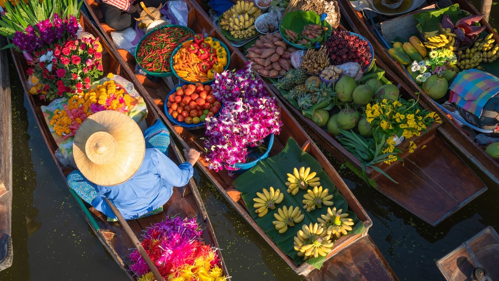 Pływający targ w Tajlandii, na którym ludzie sprzedają owoce i żywność na drewnianych łodziach, jest popularną atrakcją turystyczną