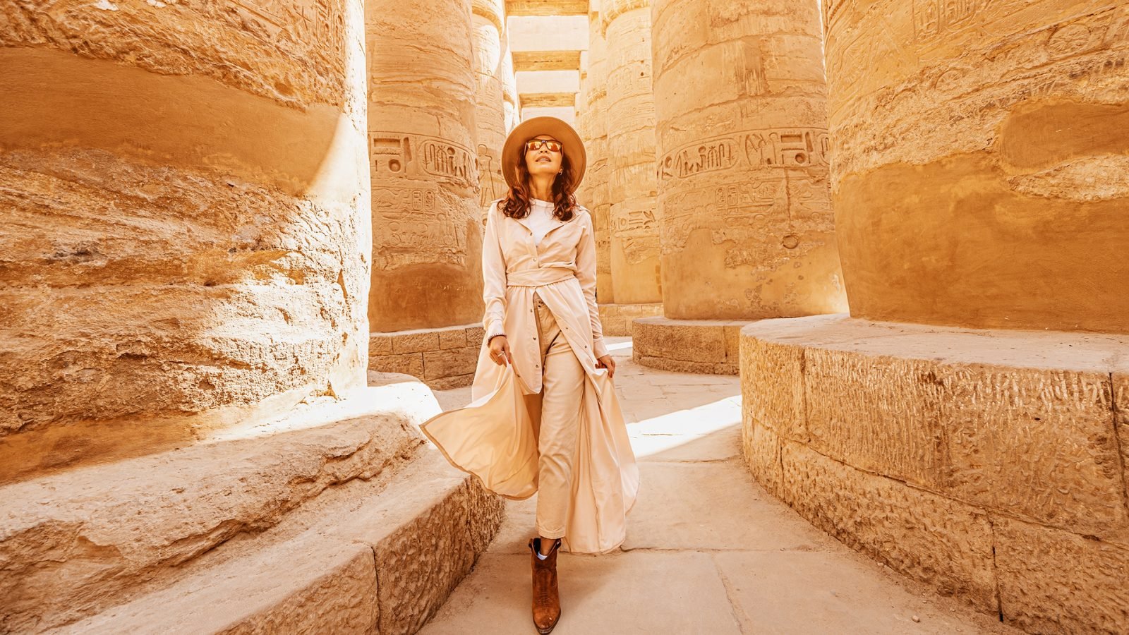 Szczęśliwa podróżniczka zwiedza ruiny starożytnej świątyni Karnak w zabytkowym mieście Luksor w Egipcie. Olbrzymi rząd kolumn z rzeźbionym hieroglifem.