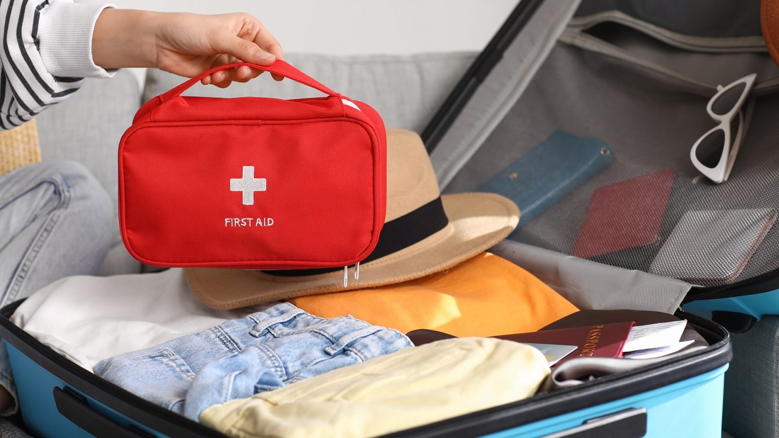 Młoda kobieta z walizką i apteczką na kanapie w domu, zbliżenie.