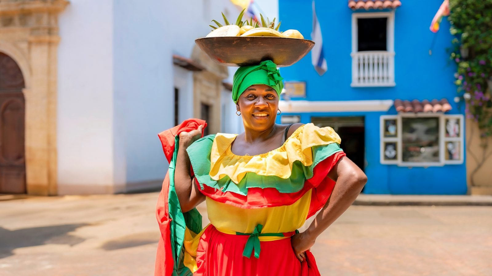 Afro-Latynoska Palenquera w kolorowej, czerwono-żółto-zielonej sukience z rozłożoną spódnicą i misą z owocami na głowie w Cartagenie w Kolumbii. Palenqueras są symbolami afrokolumbijskiego dziedzictwa.