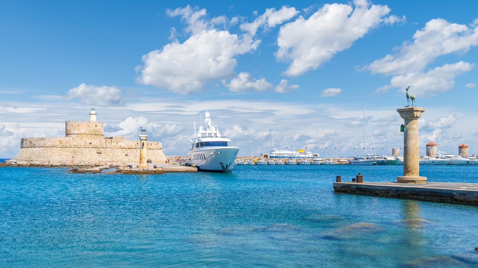 Malowniczy widok na port Mandraki na wyspie Rodos w Grecji, z twierdzą św. Mikołaja i Kolosem Rodyjskim.