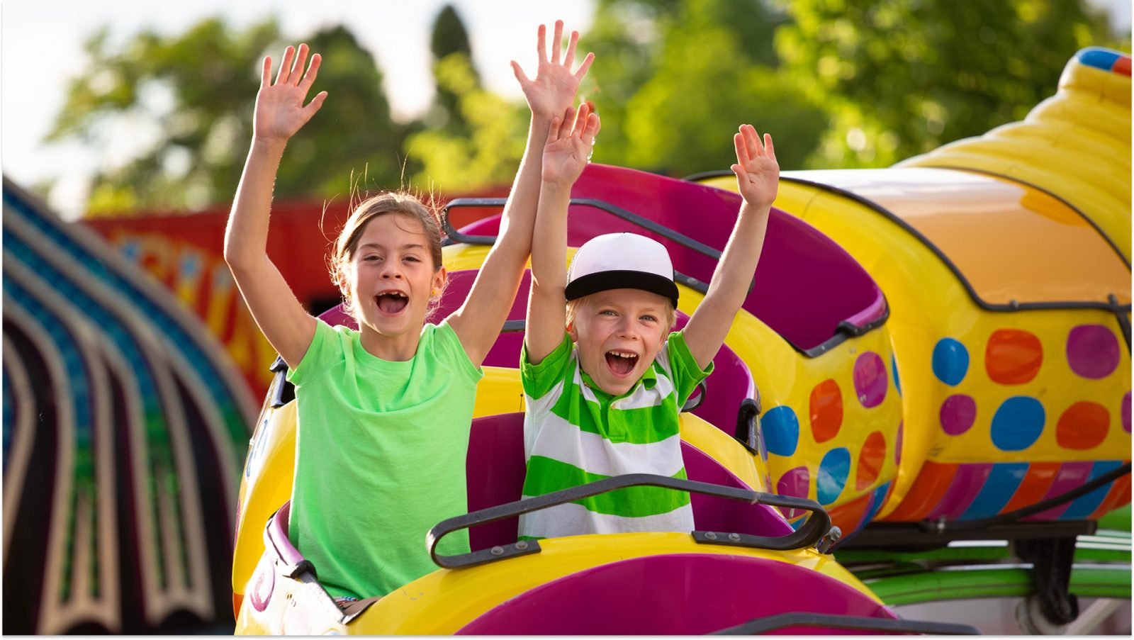 Chłopiec i dziewczynka na ekscytującej przejażdżce kolejką górską w parku rozrywki, z uniesionymi rękami i krzyczącymi z ekscytacji. Zdjęcie koncepcyjne letniej zabawy.