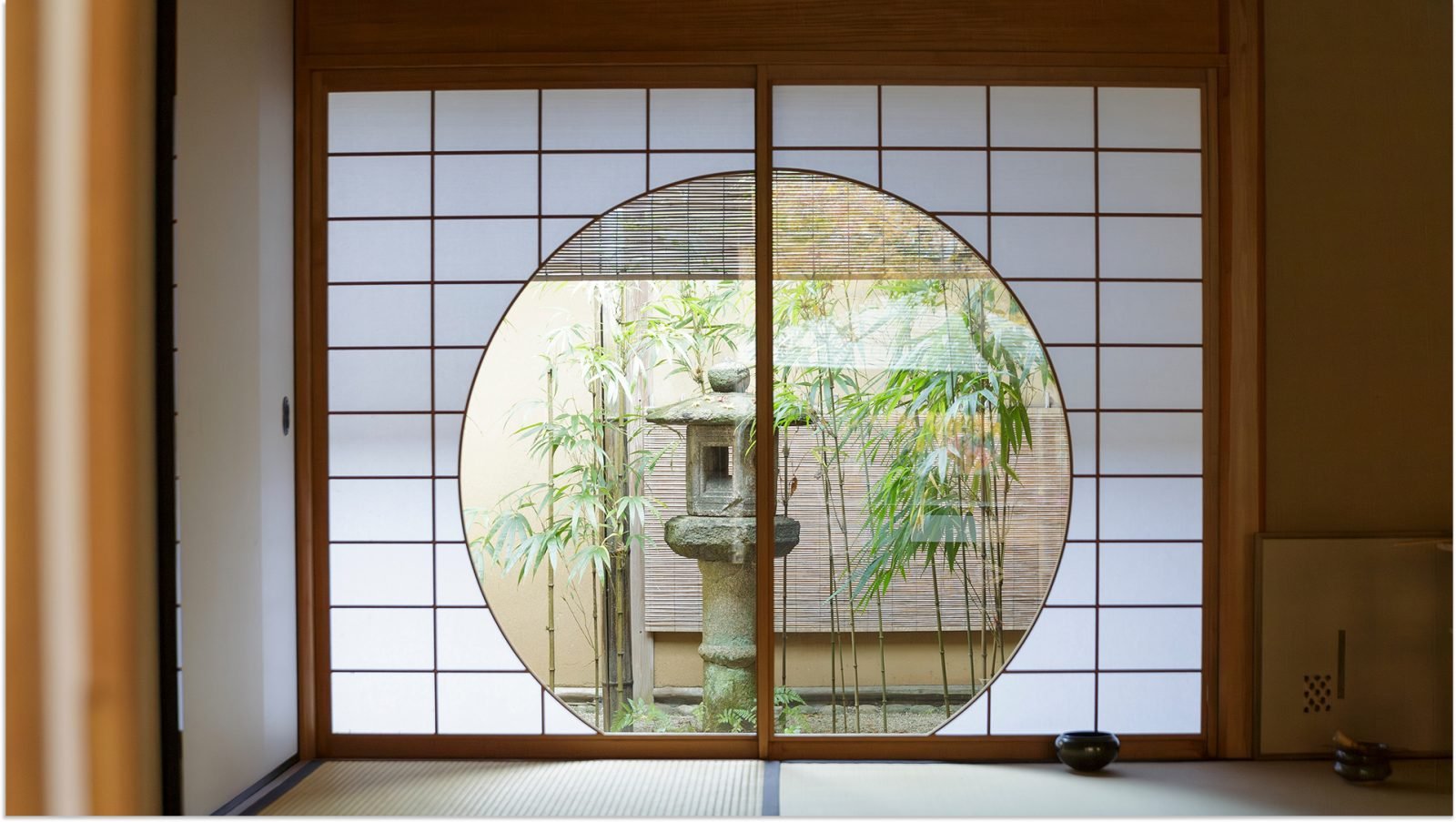 Herbaciarnia z okrągłym oknem z widokiem na bambusy i kamienną rzeźbę