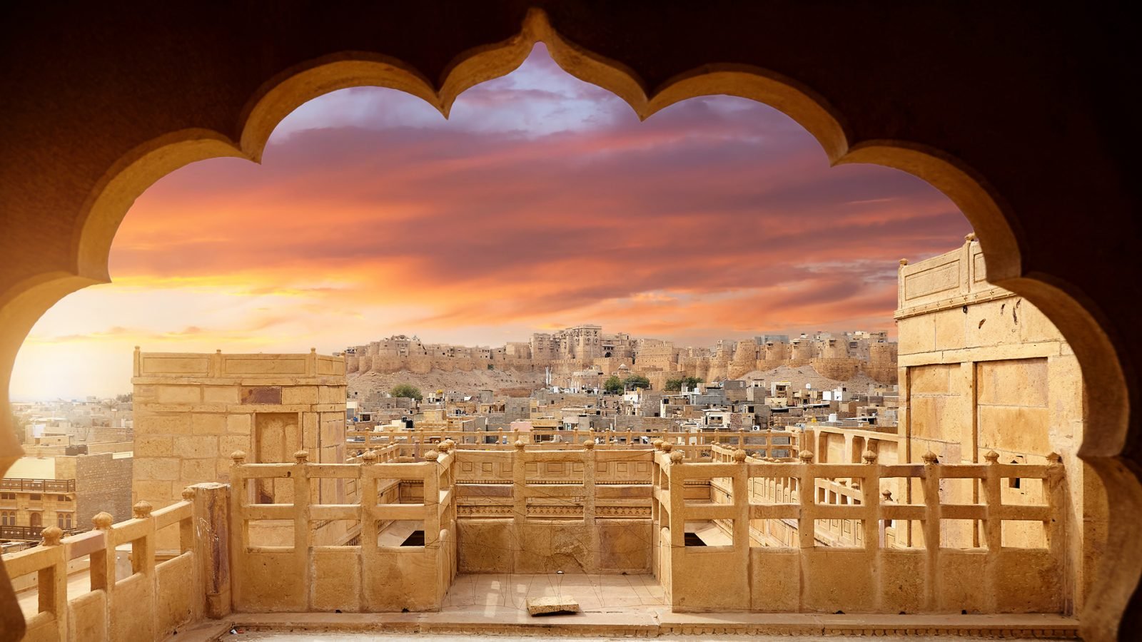 Fort w Dżajsalmerze w otoczeniu fioletowego zachodu słońca i sylwetki łuku w piaskowcowym mieście pustynnym w Radżastanie w Indiach.